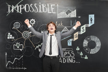 Happy and cheerful man standing on dark chalkboard . Colorful symbols and graphs painted on it. Concept for success in lifeの写真素材