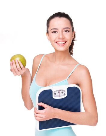 Smiling fit beautiful woman holding weighs and apple, isolated on white の写真素材