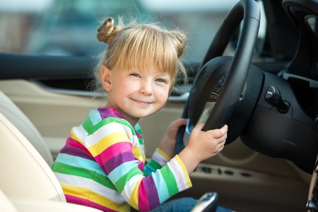 Cute little girl sitting inside car and pretending to drive it. Concept for car rentalの写真素材