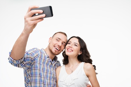 Boyfriend and girlfriend making selfie on phone. They look happy. Isolated on white backgroundの写真素材