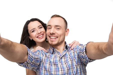 Boyfriend and girlfriend making selfie on phone. They look happy. Isolated on white backgroundの写真素材