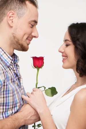 Man giving red rose to his beloved. Woman smiling. She is pleased to receive a gift. Isolated on white backgroundの写真素材
