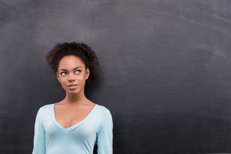 Photo of beautiful young afro-american woman on blank chalkboard background. Woman smiling and looking asideの写真素材