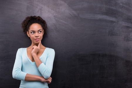 Photo of young afro-american woman on blank chalkboard background. Woman smiling and looking asideの写真素材