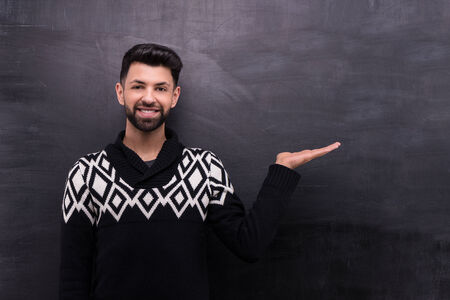 Photo of handsome young stylish man on blank chalkboard background. Man smiling and presenting somethingの写真素材