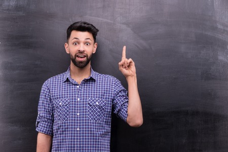 Photo of handsome young casual man on blank chalkboard background. Man excitedly pointing at somethingの写真素材