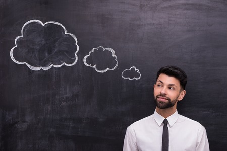Photo of handsome young businessman on chalkboard background. Man looking at cloud formed dialogの写真素材