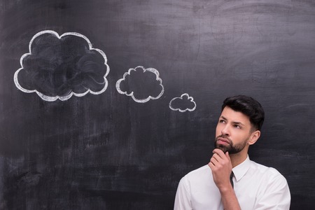 Photo of handsome young businessman on chalkboard background. Man thoughtfully looking at cloud formed dialogの写真素材