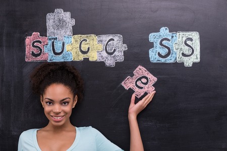 Young afro-american woman on chalkboard background smiling and looking at camera. Painted puzzles are on chalkboard. Concept for successの写真素材