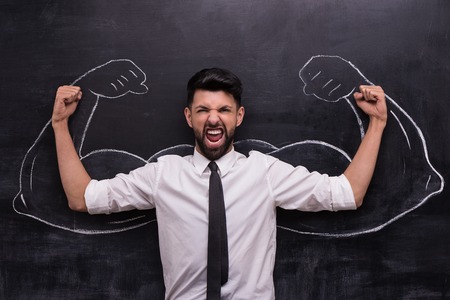 Funny picture of young businessman ready to win on chalkboard background. Two strong muscular arms painted on chalkboardの写真素材