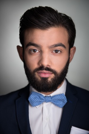 Photo of handsome stylish man with beard. Man wearing classic dark blue suit and a blue bow tie. Man seriously looking at cameraの写真素材