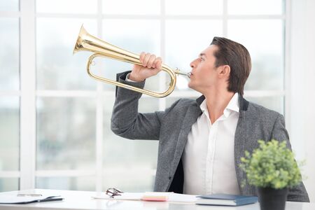 Young businessman playing the trumpet. Office interior with big windowの写真素材