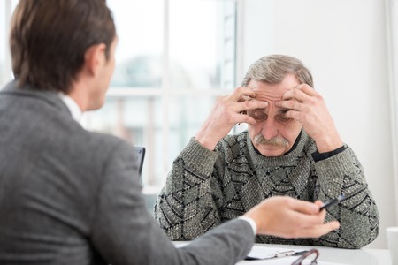 Young businessman having an interview or business meeting with sad old man. Office interior with big windowの写真素材