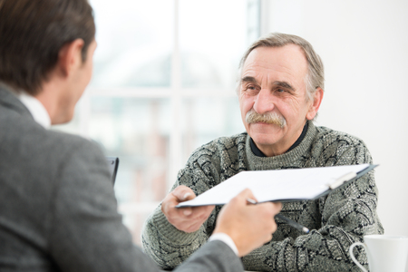 Young businessman having an interview or business meeting with smiling old man. Office interior with big windowの写真素材
