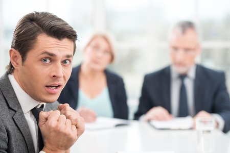 Young scared man having an interview or business meeting with employers. Office interior with big windowの写真素材