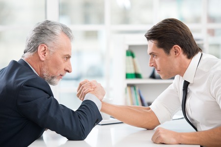 Two businessmen doing arm wrestling. Old one winning. Office interior with big windowの写真素材