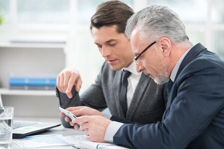 Two businessmen working with documents and tablet computer. Office interior with big windowの写真素材