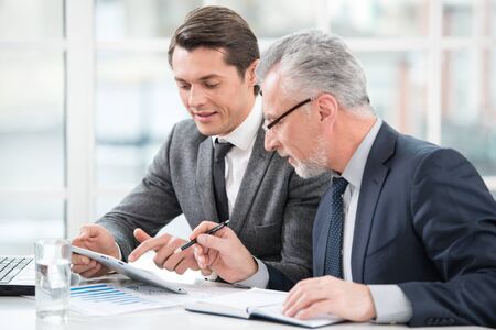 Two businessmen working with documents and tablet computer. Office interior with big windowの写真素材