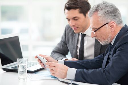 Two businessmen working with documents and tablet computer. Office interior with big windowの写真素材
