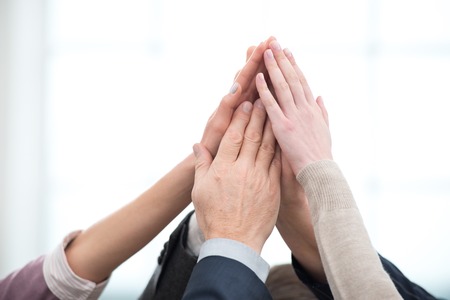 Close up photo of business team holding hands to hands. Office interior with big windowの写真素材