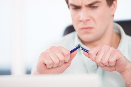 Close up of young angry businessman breaking blue pencil. Office interior with windowの写真素材