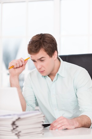 Young tired businessman looking at papers and folders while sitting at his black leather office chair. Office interior with windowの写真素材