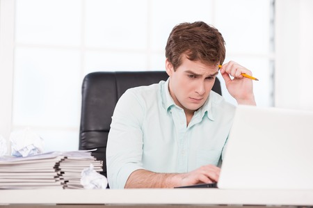 Young sad businessman looking at papers and folders while sitting at his black leather office chair. Office interior with windowの写真素材