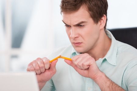 Close up of young angry businessman breaking pencil. Office interior with windowの写真素材