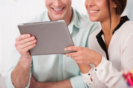Close up photo of young creative businessman and mixed race businesswoman working with tablet computer. Office interior with windowの写真素材