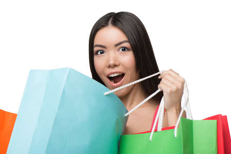 Close up of asian surprised young woman looking at camera. She holding colorful paper bags. Concept for shop sales. Isolated on white backgroundの写真素材