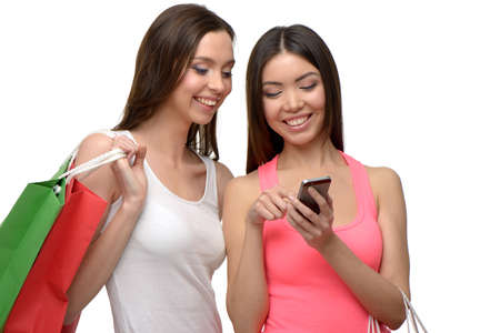 Two young women with colorful paper bags. They using phone. Concept for shop sales. Isolated on white backgroundの写真素材