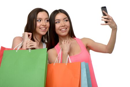 Two young women with colorful paper bags. They smiling and using phone. Concept for shop sales. Isolated on white backgroundの写真素材