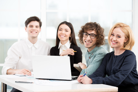 Business team looking at camera while working with laptop. Office interior with window. Concept for teamworkの写真素材
