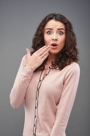 Surprised young woman looking at camera, standing on grey backgroundの写真素材