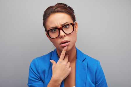 Young mixed race woman with thoughtful glance wearing glasses, standing on grey backgroundの写真素材