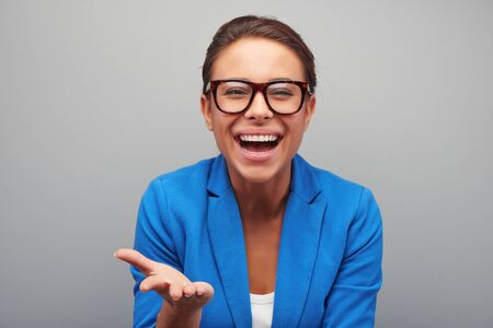 Young mixed race woman with glasses cheerfully smiling, standing on grey backgroundの写真素材