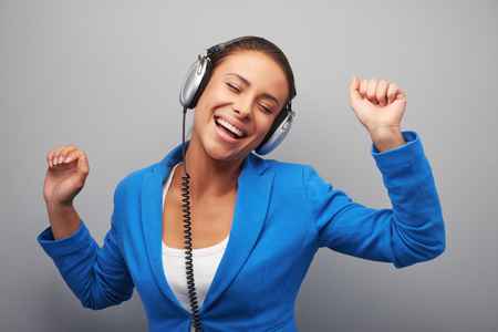 Young mixed race woman with headphones listening music amusedly, standing on grey backgroundの写真素材