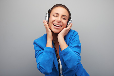 Young mixed race woman with headphones listening music gladly, standing on grey backgroundの写真素材