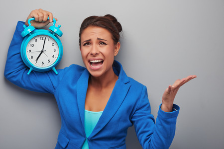 Awaken mixed race woman holding alarm clock, standing on grey backgroundの写真素材