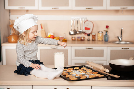 Little cute girl with chef hat preparing cookies. Kitchen interior. Concept for young kitchen handsの写真素材