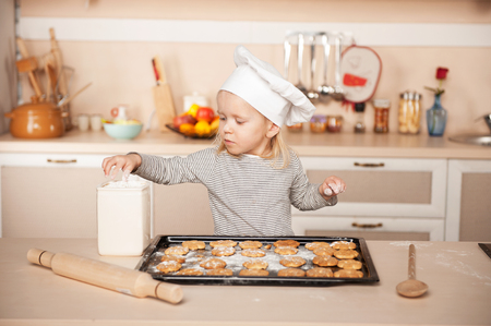 Little cute girl with chef hat preparing cookies. Kitchen interior. Concept for young kitchen handsの写真素材