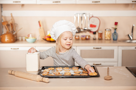 Little cute girl with chef hat preparing cookies. Kitchen interior. Concept for young kitchen handsの写真素材