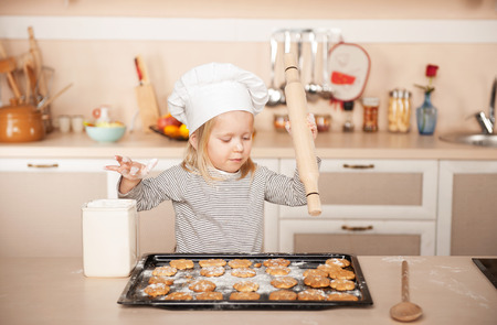 Little cute girl with chef hat and rolling pin preparing cookies. Kitchen interior. Concept for young kitchen handsの写真素材
