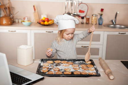 Little cute girl preparing cookies. Kitchen interior with laptop on the table. Concept for young kitchen handsの写真素材