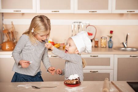 Little cute girl feeding her older sister cake. Kitchen interior. Concept for young kitchen handsの写真素材