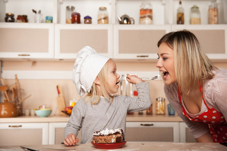 Little cute girl feeding her mother cake. Kitchen interior. Concept for young kitchen handsの写真素材