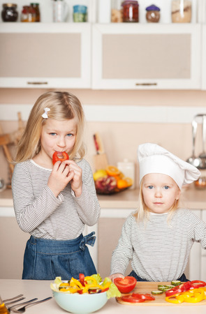 Little cute girls trying to cook salad and help their mother. Kitchen interior. Concept for young kitchen handsの写真素材