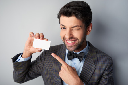 Portrait of positive casual young man wearing jacket and bow tie. Man smiling and pointing at blank visiting cardの写真素材