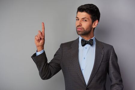 Portrait of elegant casual young man wearing tweed jacket and bow tie. Man pointing up and looking at cameraの写真素材