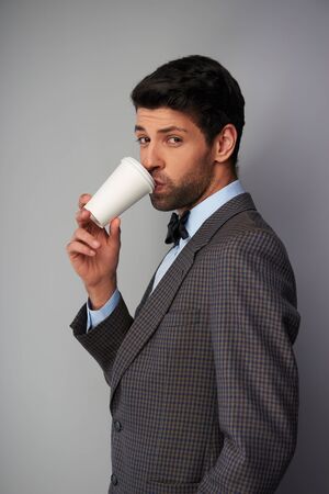 Portrait of elegant casual young man wearing tweed jacket and bow tie. Man drinking coffee in a white cup and looking at cameraの写真素材